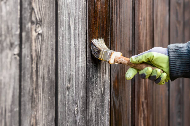 Brushing dark stain onto weathered fence boards